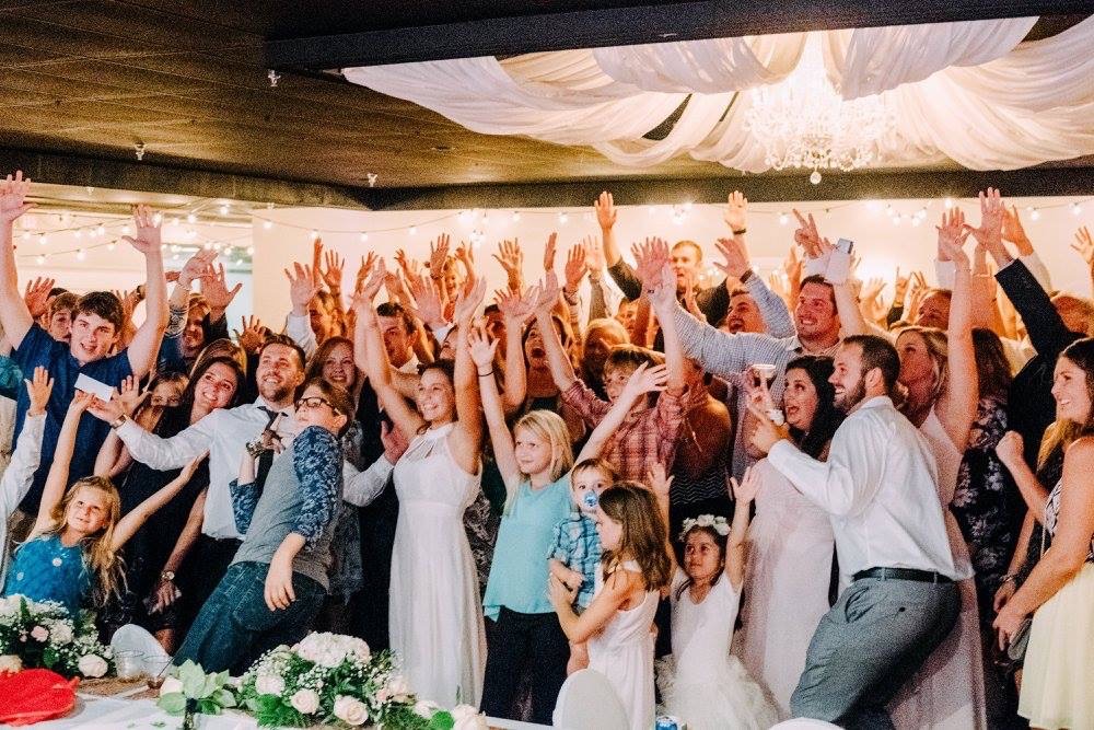 Group of people dressed up at a wedding with hands up in the air smiling.